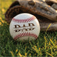A white baseball resting on green grass with a brown baseball glove blurred in the background. The baseball is printed with the word 'DAD' in large brown letters and three names underneath: 'Olivia', 'Dan', and 'Sam'.