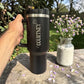 Black travel mug with Courtney branding held by a hand, next to a small jar of flowers on a wooden surface. Stanley 40oz
